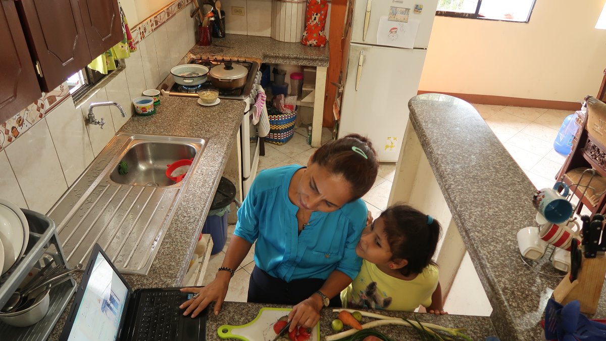 La profesora Carmita Agurto participa en una reunión de la escuela mientras atiende a una de sus hijas.