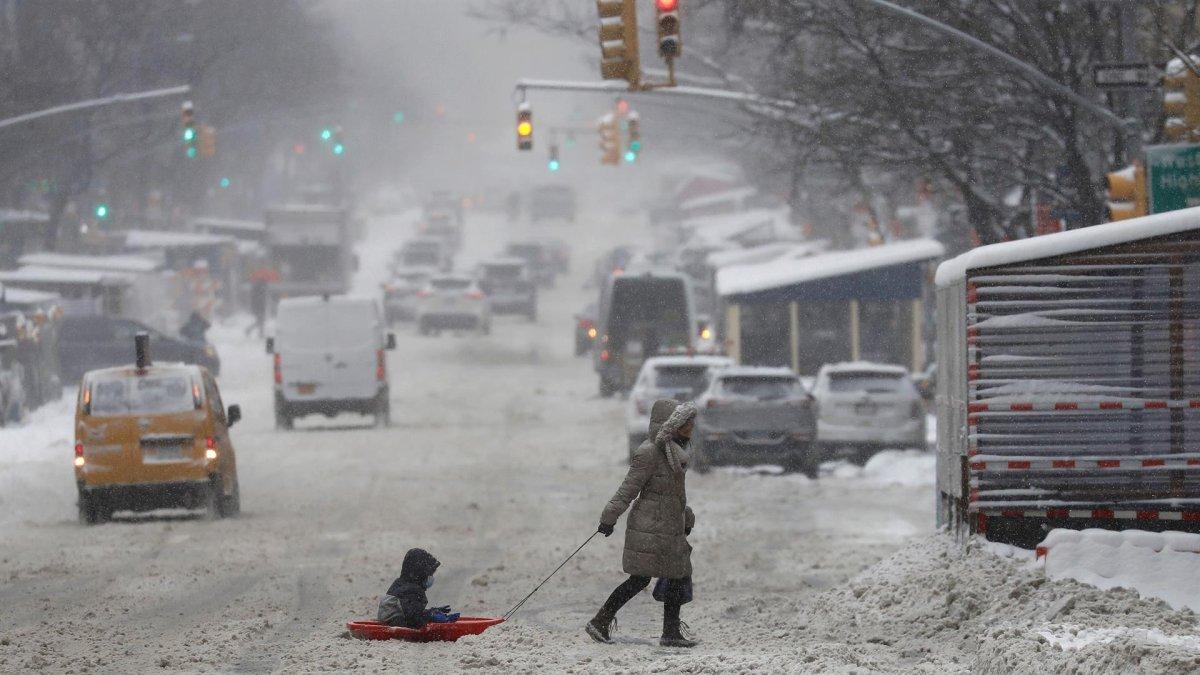Una mujer y un niño sobre un trineo fueron registrados este sábado al cruzar una calle cubierta de nieve en Nueva York (NY, EE.UU.).