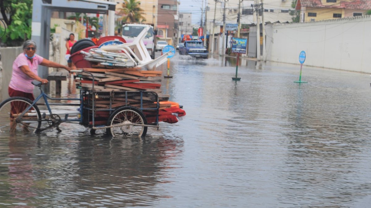 Una comerciante intenta avanzar en medio del agua, con su triciclo rumbo a la playa.,