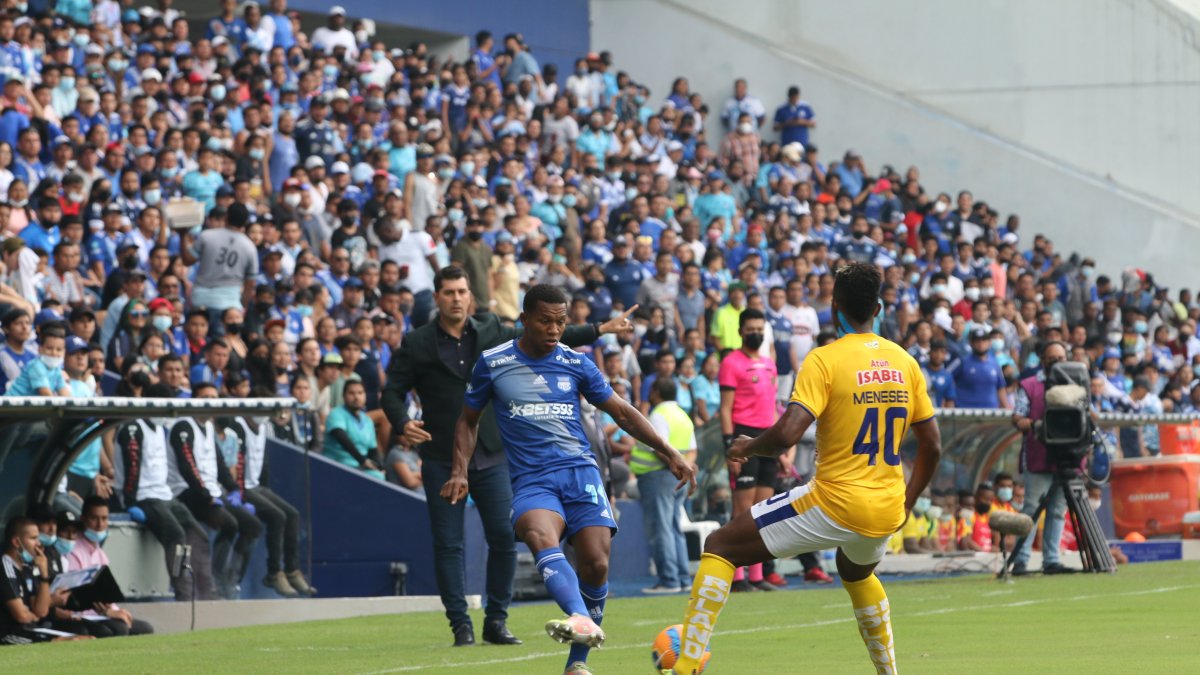 Romario Caicedo, jugador de Emelec, domina el balón mientras Ismael Rescalvo, entrenador azul, sigue la acción.