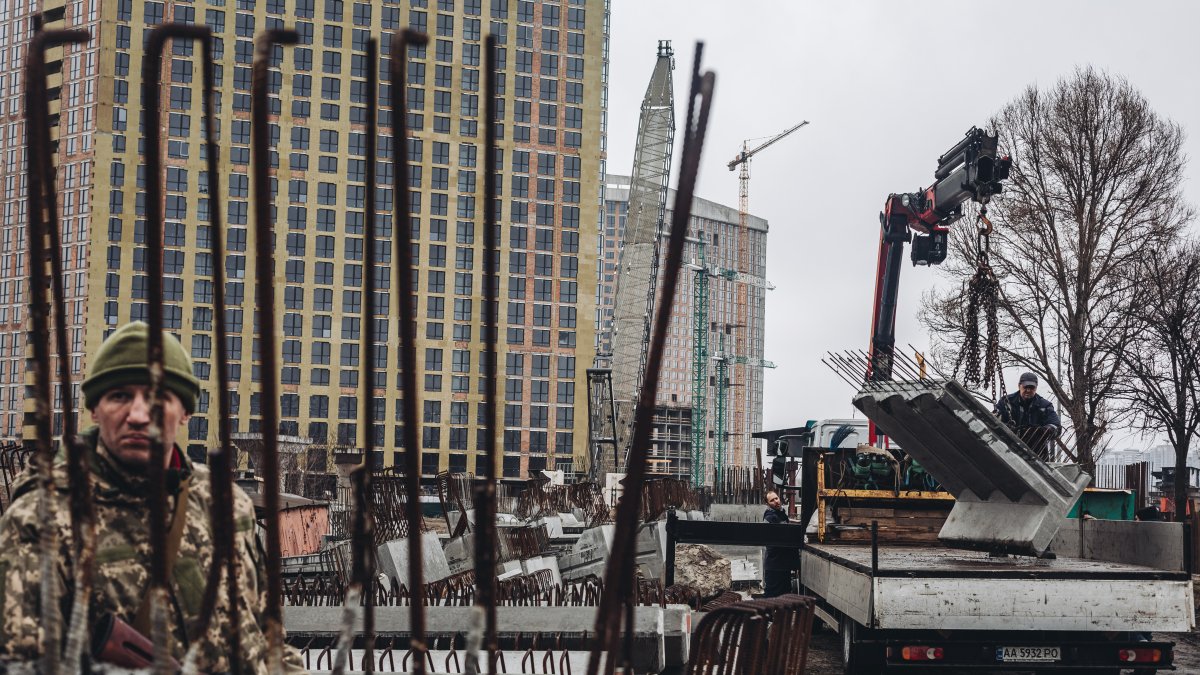 Varios operarios cargan losas de cemento frente a un miliciano ucraniano
