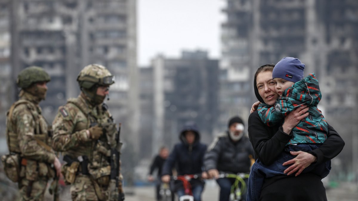 Mariúpol.  Varios civiles caminan, mientras militares ucranianos resguardan una avenida en esta ciudad puerto.