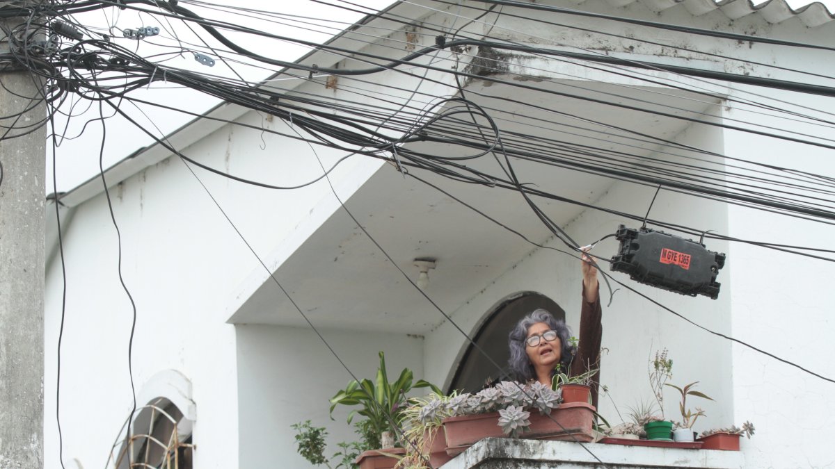 Marisol Paredes, quien reside en la manzana 207 de Guayacanes, muestra la hilera de cables que cruzan el balcón de  su casa. Muchos de ellos no tienen ninguna función, pero nadie los ha ido a retirar.