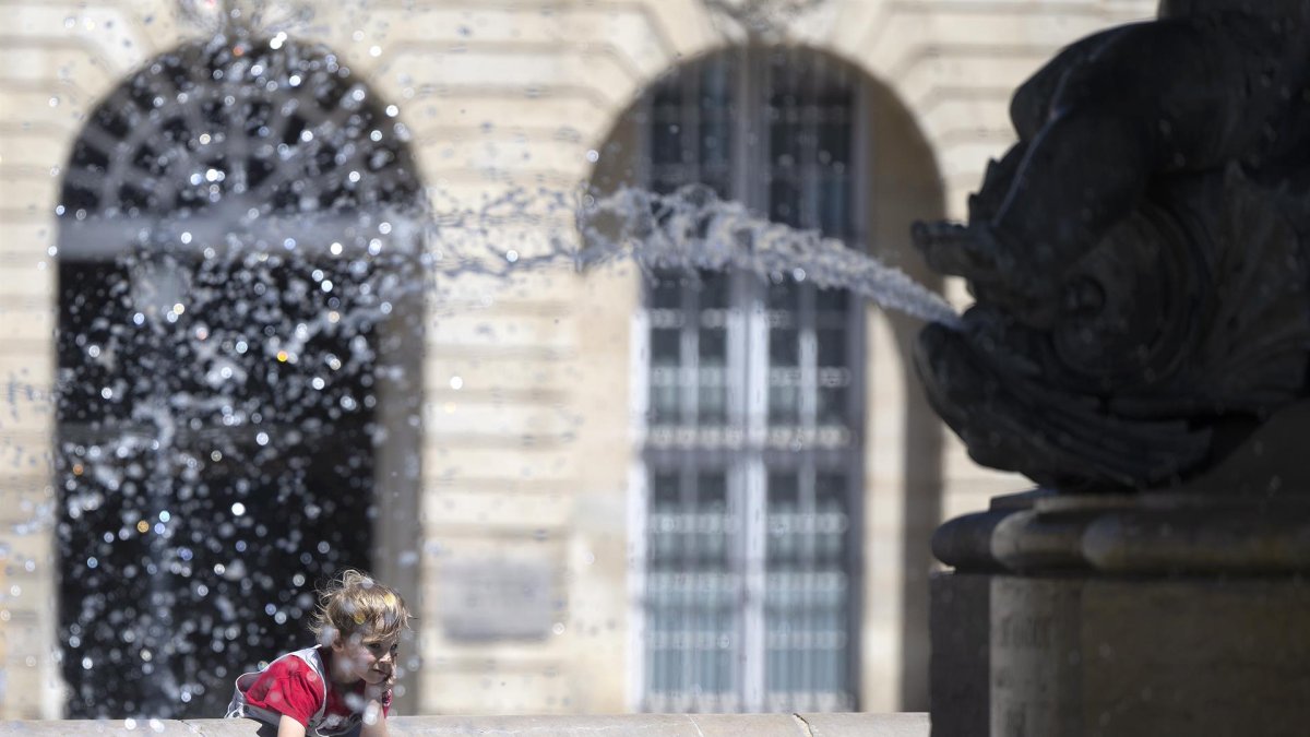 Un niño se rocía con agua de la fuente en la Place de la Bourse, durante la ola de calor, en la ciudad francesa de Burdeos.