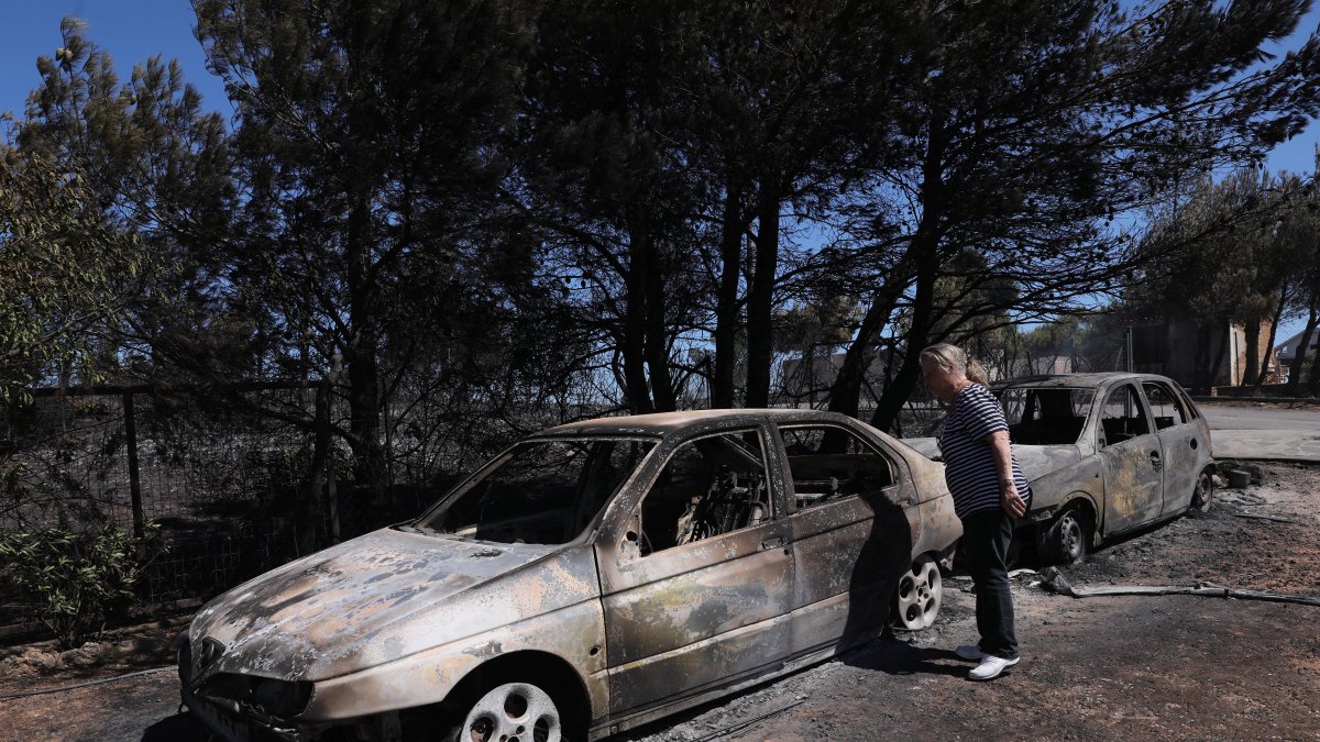 Una mujer observa los coches quemados del incendio acaecido en Anthousa, cerca de Atenas, Grecia.