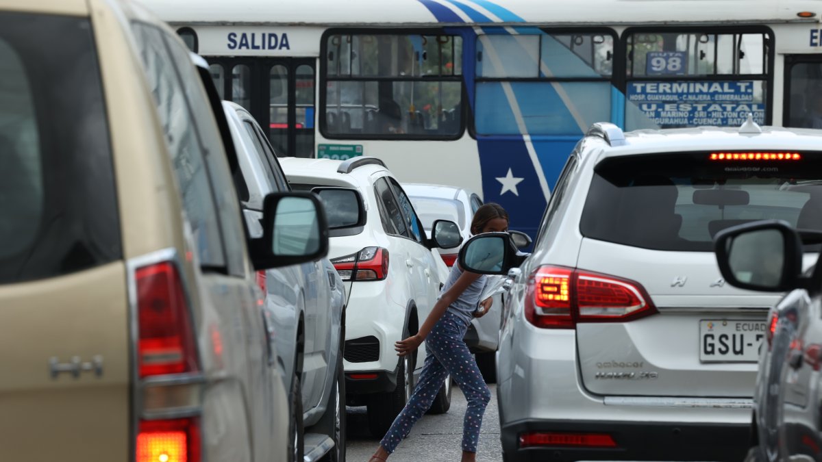 Una  niña esquiva los autos del tráfico mientras intenta comercializar fundas de basura.