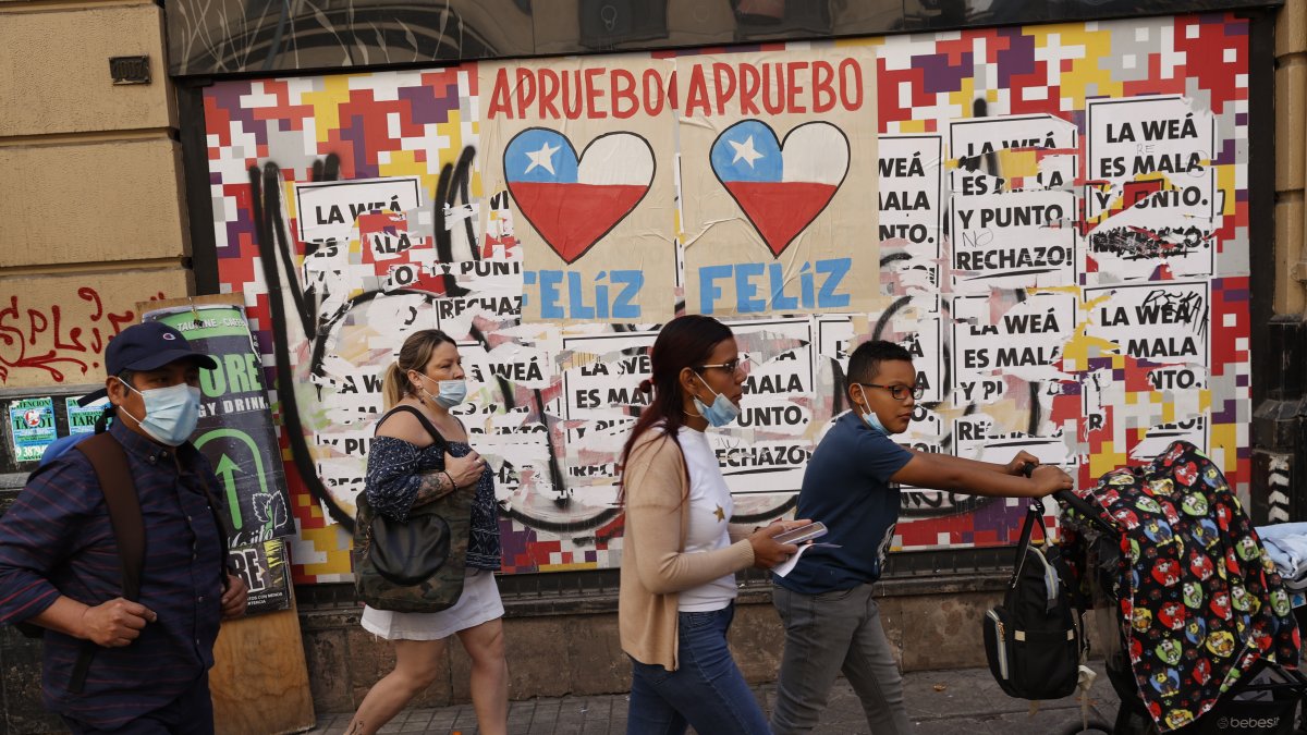 Varias personas caminan frente a una pared con información relacionada al plebiscito constitucional en Santiago (Chile).
