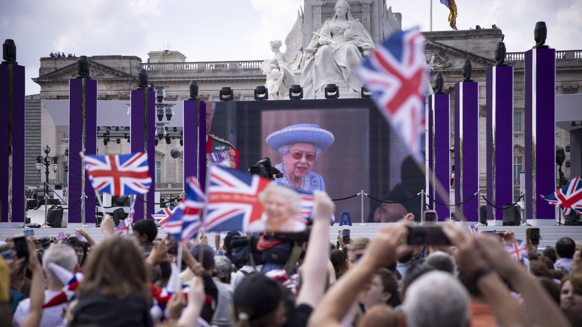 Londres. Gente en un centro comercial viendo a Su Majestad, en el balcón del Palacio de Buckingham mostrado en una pantalla grande durante las celebraciones del Jubileo, el 2 de junio de 2022.