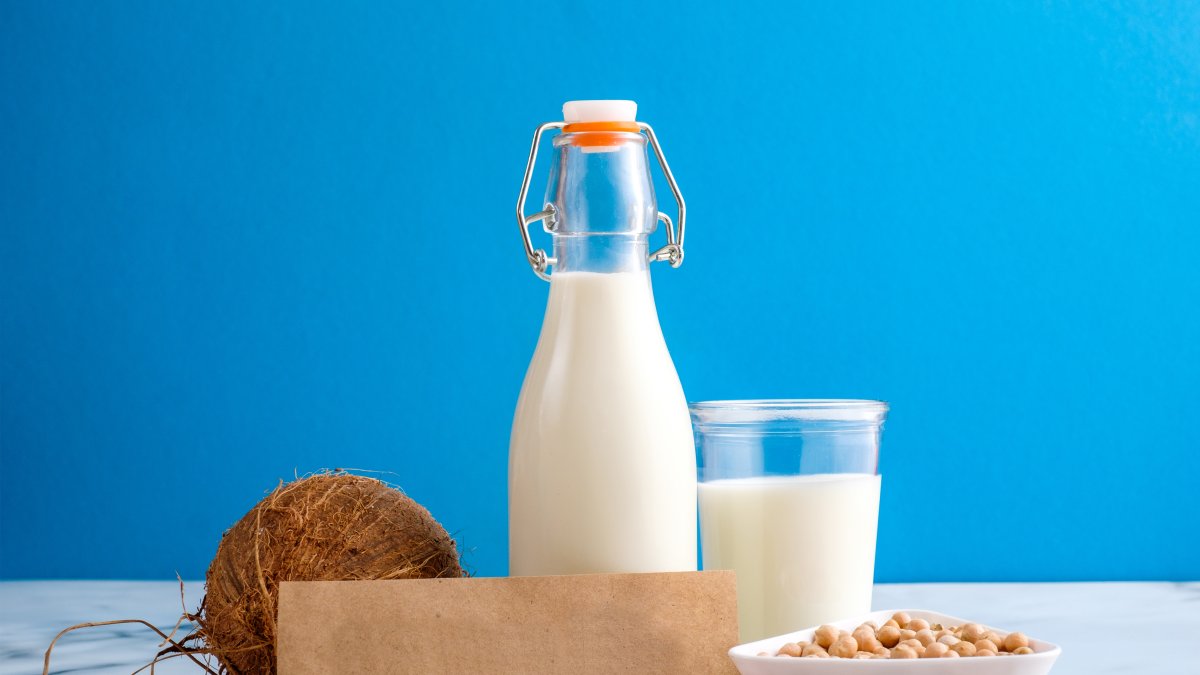 Lactose free milk. Bottle and glass of milk, almond nuts, oat flakes, coconut and piece of paper with text LACTOSE FREE on wooden surface on blue background. Lactose intolerance food concept