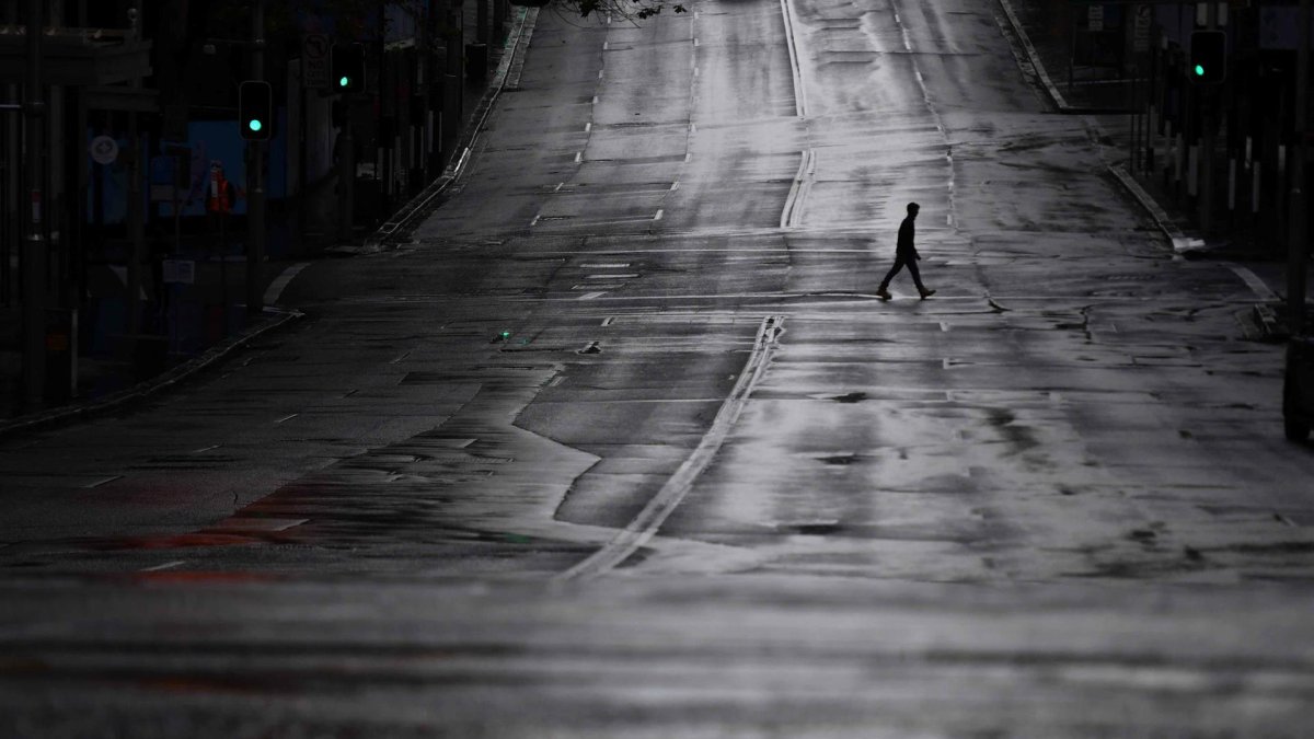 Fotografía de archivo de un transeúnte que cruza una calle completamente vacía en Sídney, Australia.