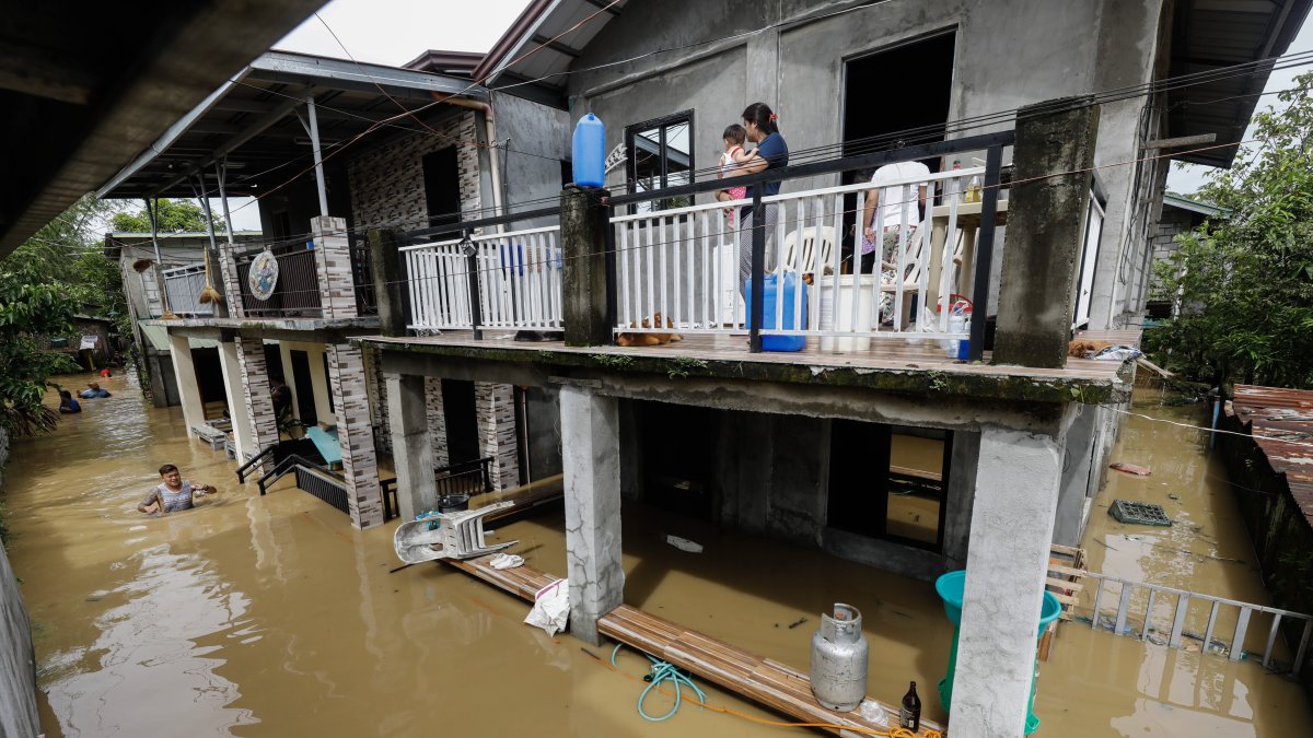 Una madre y su bebé observan desde la terraza de su vivienda completamente rodeada por el agua que anega la ciudad de San Miguel como consecuencia de las inundaciones provocadas por el tifón Noru en Filipinas. Al menos cinco personas perecieron este lunes y más de 74.000 fueron evacuadas por el paso del tifón, que tocó tierra en el noreste del archipiélago filipino con vientos de hasta 185 kilómetros por hora y que ya ha abandonado la isla de Luzón en dirección oeste. EFE/ Rolex Dela Pena