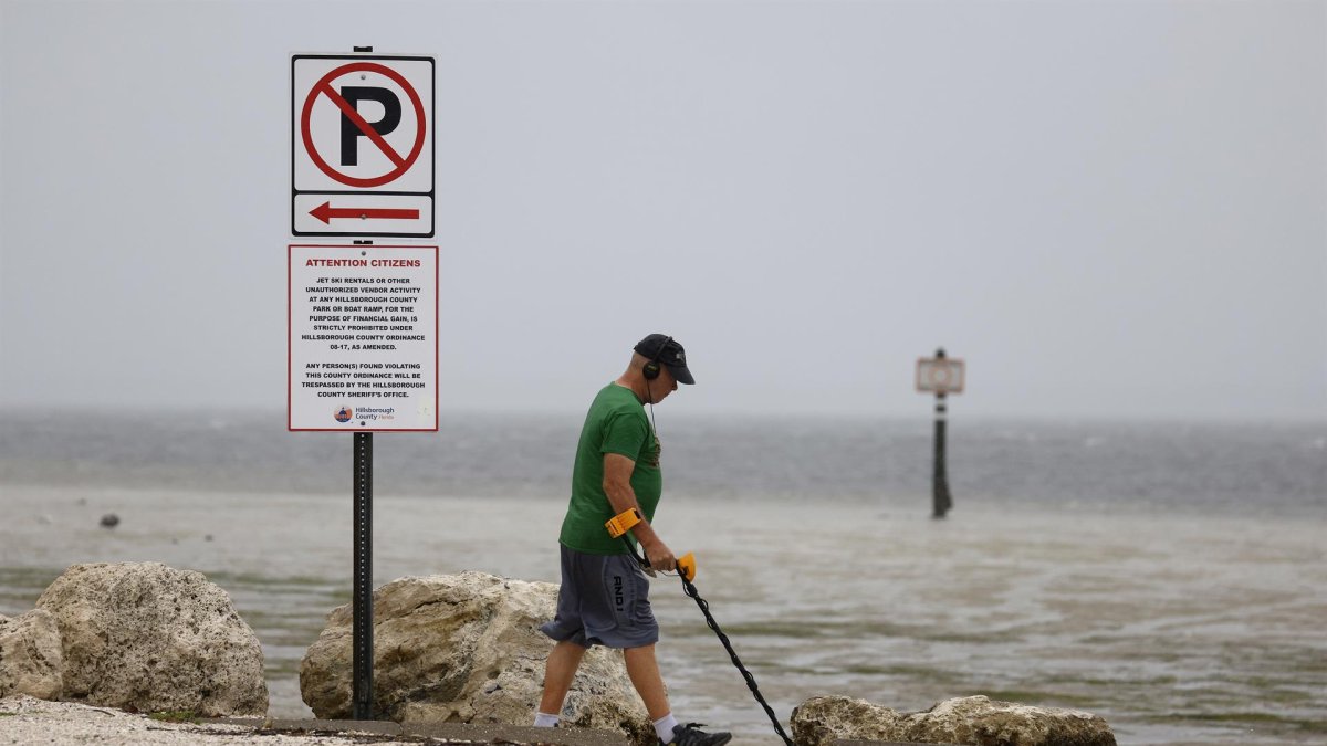 Un hombre camina con un detector de metales por lo que los lugareños reportaron como una costa expuesta por aguas mucho más retrocedidas de lo normal ante la llegada del huracán Ian, en Clearwater, Florida.