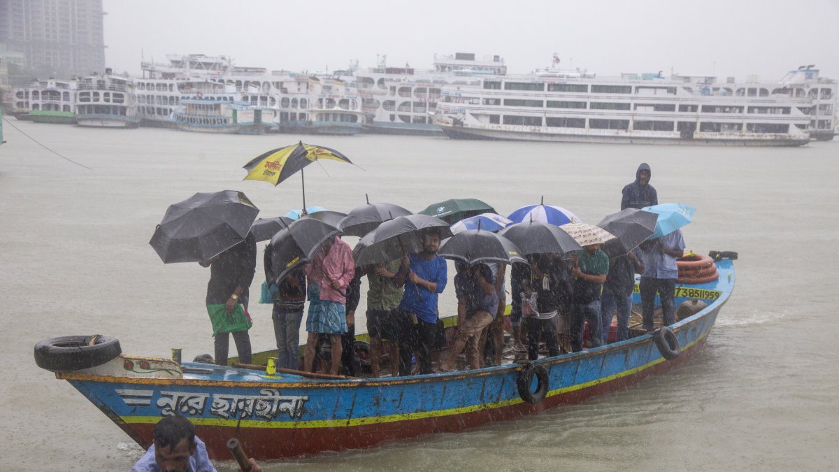Los pasajeros de Bangladesh cruzan el río Buriganga mientras sostienen paraguas durante una fuerte lluvia y las duras condiciones causadas por el ciclón Sitrang. EFE /