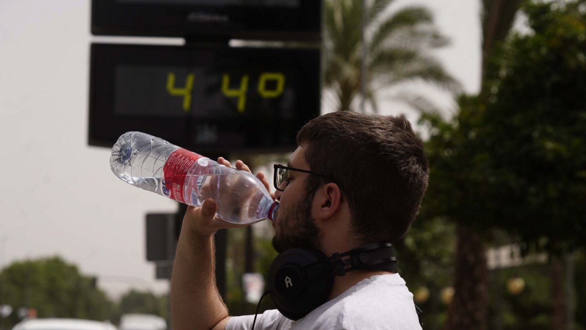 Un joven bebe agua junto a un termómetro de calle que marca 44º, en una fotografía de archivo.