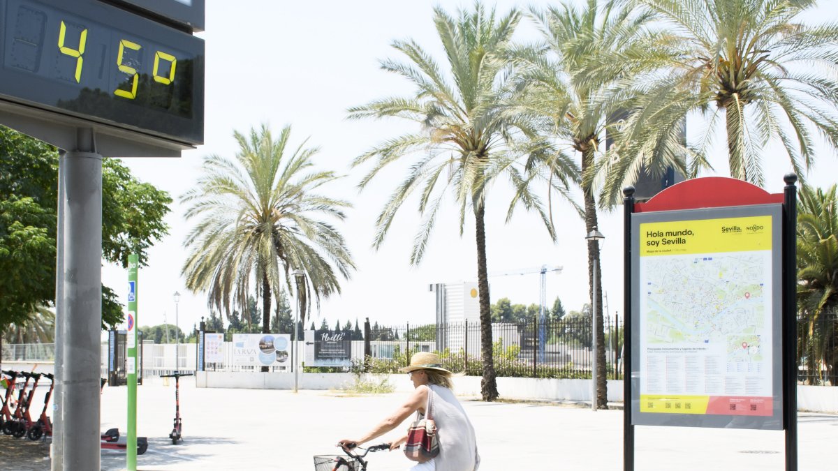Sevilla. Una mujer en bicicleta pasa junto a un termómetro que marca 45 grados en una calle de esta urbe.