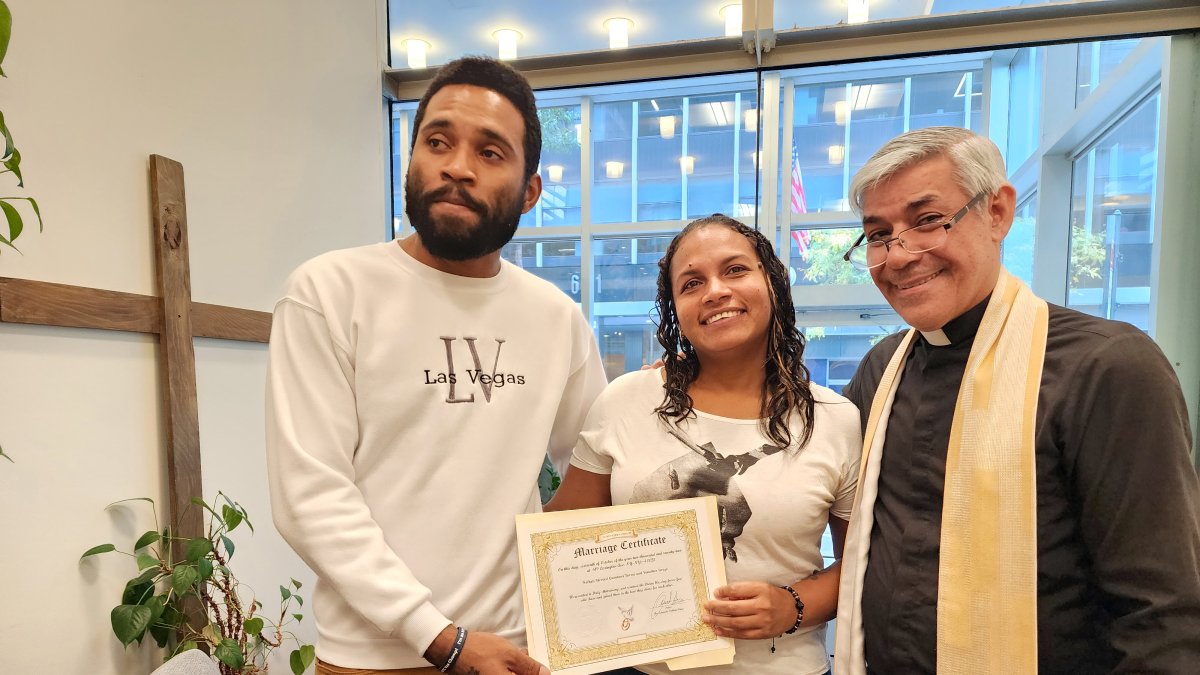 Los migrantes venezolanos Yonaiker Brujo y Nathalie Quintana muestran el certificado de matrimonio junto al sacerdote luterano, el padre Fabián Arias, en la iglesia San Pedro en Manhattan, Nueva York.
