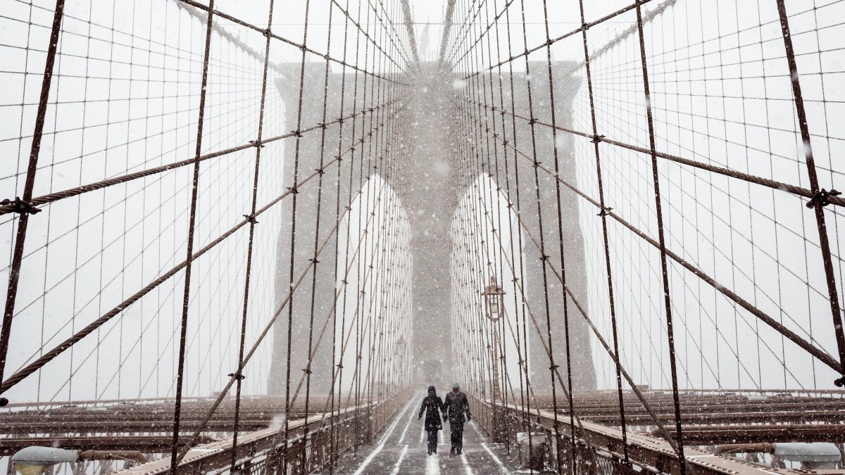 Fotografía de archivo en la que se registró a un par de transeúntes al cruzar el puente de Brooklyn, bajo una tormenta de viento y nieve, en Nueva York (NY, EE.UU.).