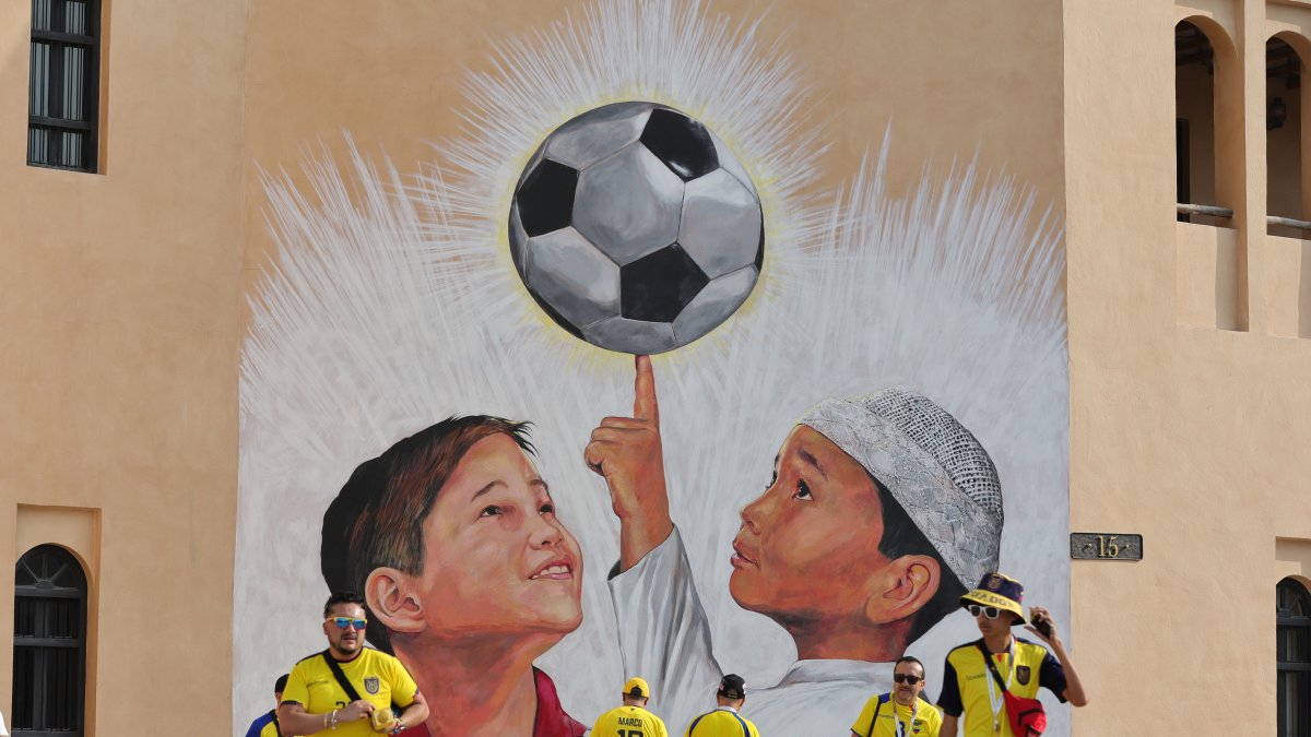 Un grupo de hinchas ecuatorianos reunidos en Qatar con una imagen alegórica al Mundial en un muro.