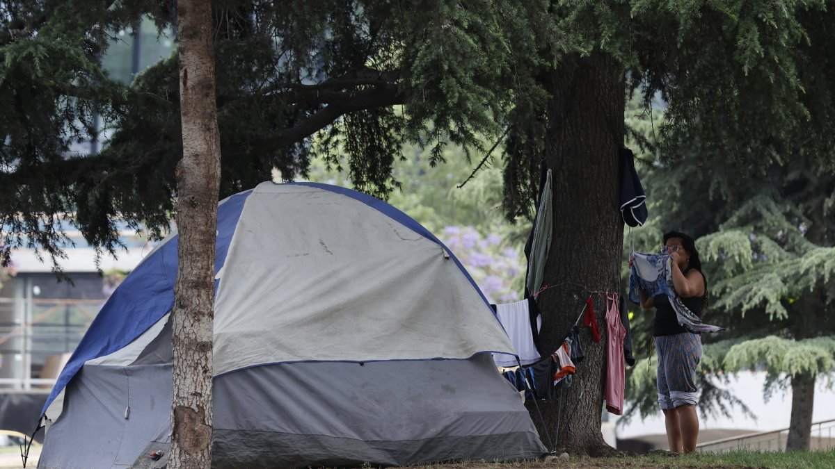 Una mujer en situación de calle cuelga su ropa en un parque público en el que acampa, hoy, en Santiago (Chile). 