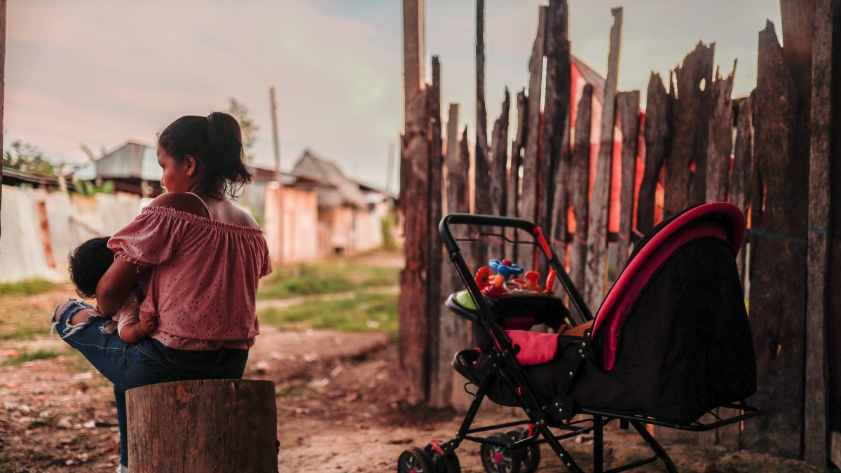 Elita se sienta afuera de su hogar para darle de lactar a su bebé, el 23 de noviembre de 2022, en Iquitos (Perú).  / Aldair Mejía