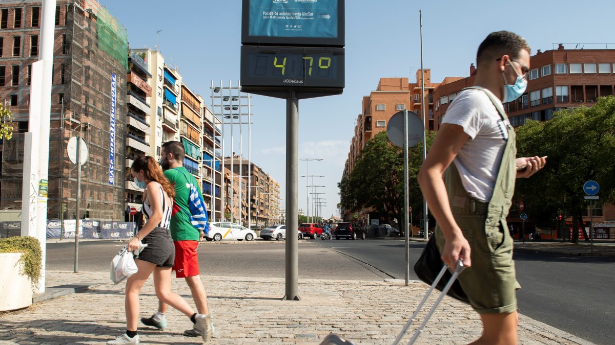 Sevilla. Varias personas pasan ante el termómetro próximo a la estación de autobuses de Plaza de Armas de esta ciudad española en un día en que las temperaturas máximas superan los 40 grados.