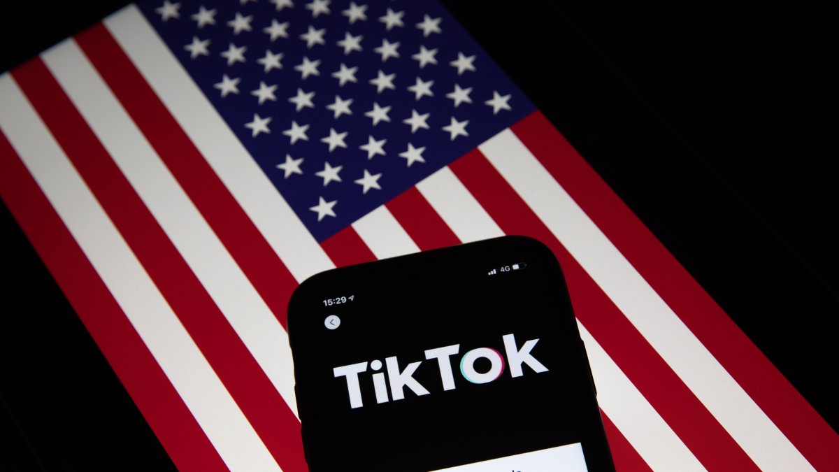 Fotografía de archivo que muestra la aplicación TikTok en la pantalla de un teléfono celular, con la bandera estadounidense de fondo.