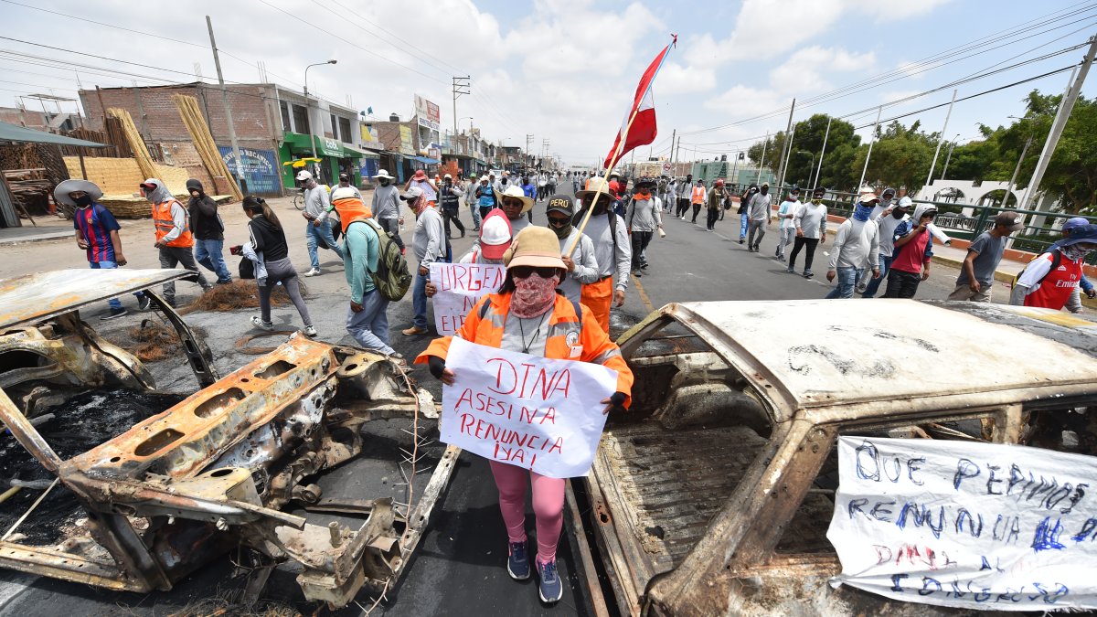 Simpatizantes de Pedro Castillo caminan entre dos vehículos incinerados mientras se manifiestan para pedir la salida de la presidenta Dina Boluarte EFE