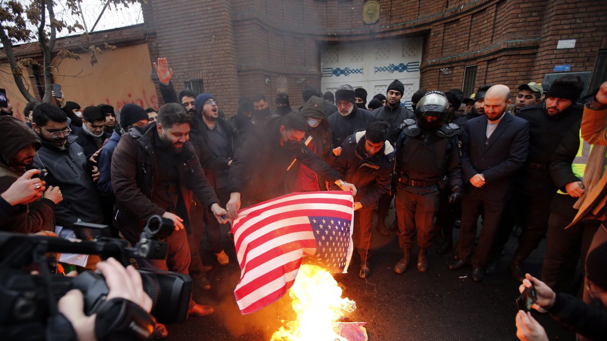 Personas queman una bandera de Estados Unidos durante una protesta frente a la embajada de Francia en Teherán.