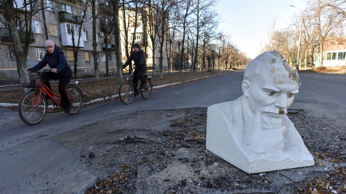 Dos personas en bicicleta pasan frente al busto de Lenin, que cubre el cráter de los bombardeos en la carretera en la ciudad recuperada de Lyman, en la región de Donetsk, en el este de Ucrania.