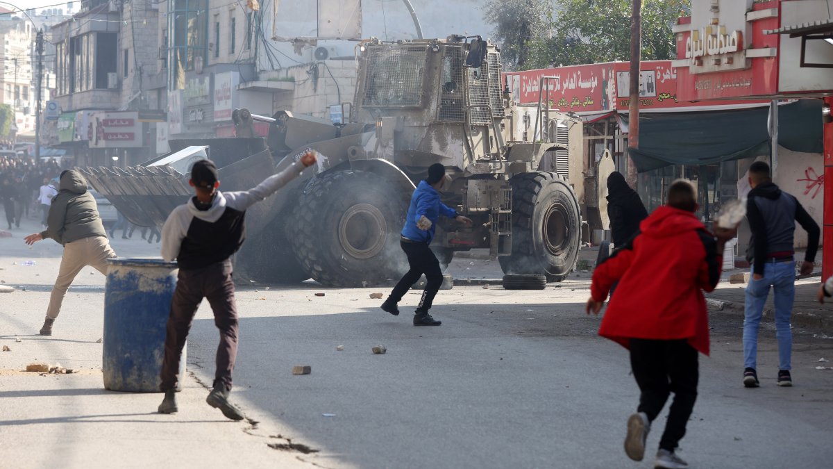 Palestinos lanzan piedras en medio de enfrentamientos con tropas israelíes durante una incursión en Yenín, Cisjordania, este 26 de enero.