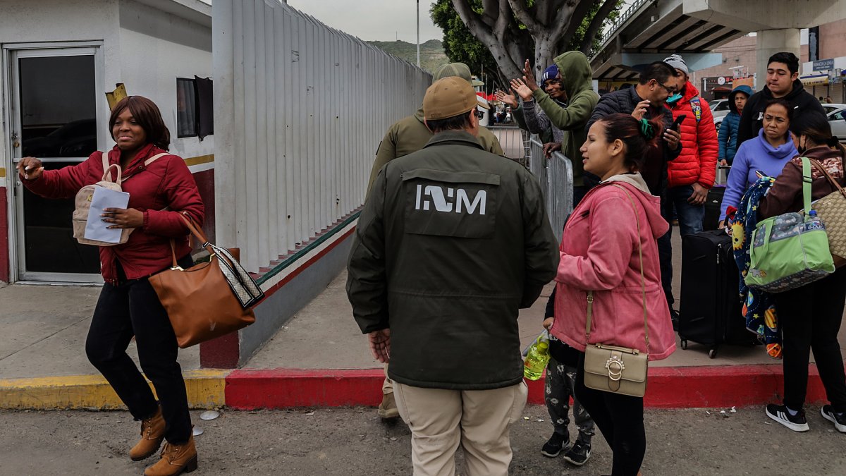 Grupos de personas migrantes hacen fila para cruzar a Estados Unidos y continuar con su proceso de asilo a través de la garita internacional del Chaparral en Tijuana.