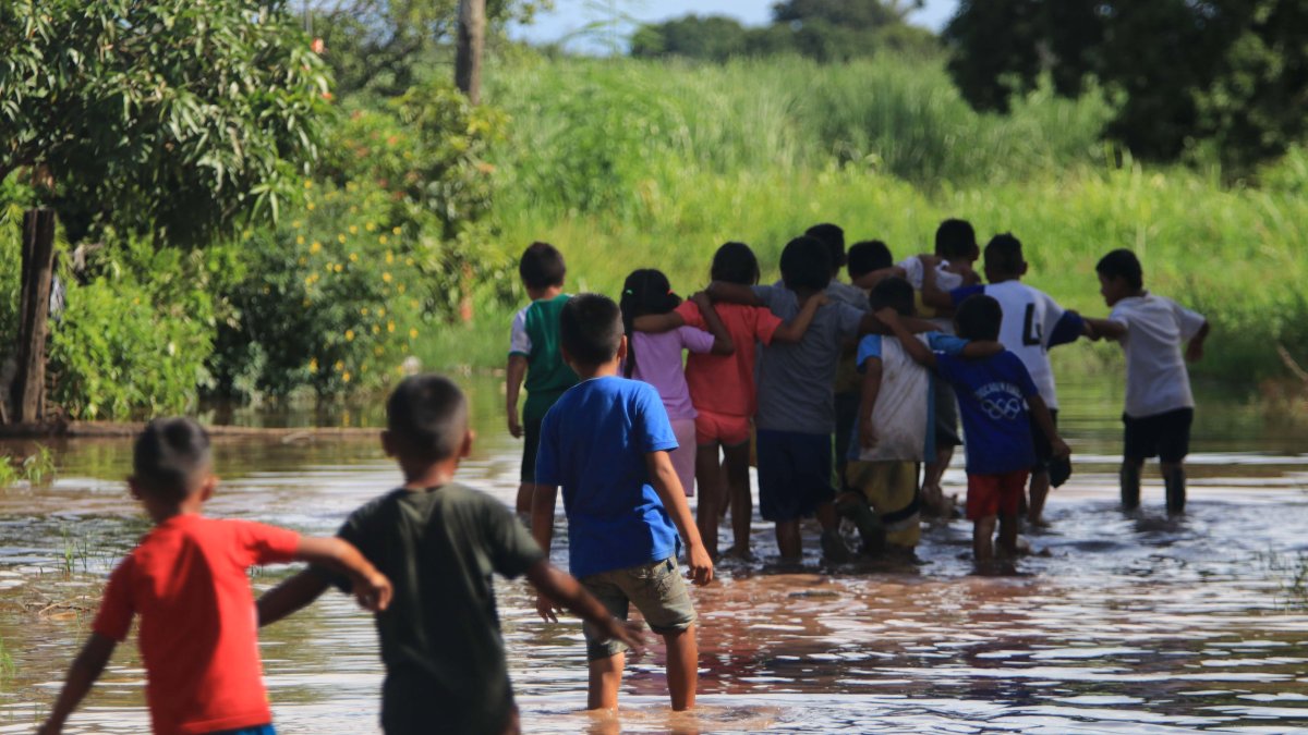Unos niños caminan en medio de una inundación en la comunidad Rancho Chico perteneciente al municipio de Okinawa.