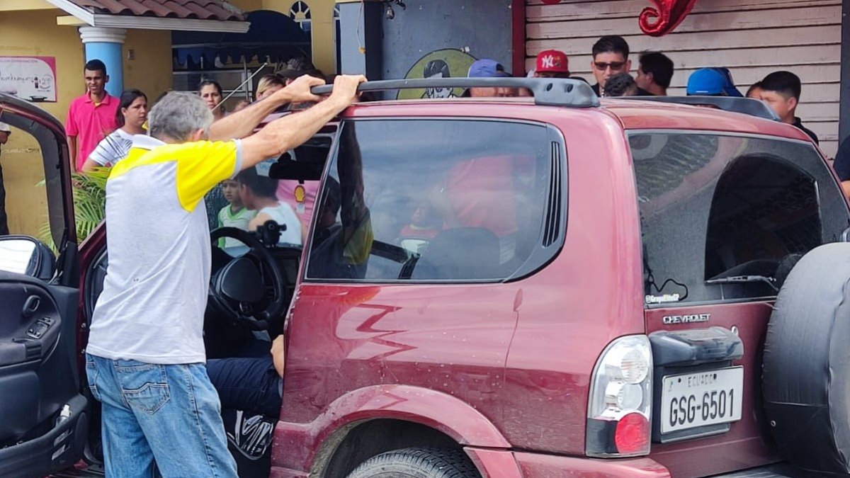 Allegados y curiosos observan el cadáver de un hombre baleado dentro de su vehículo.