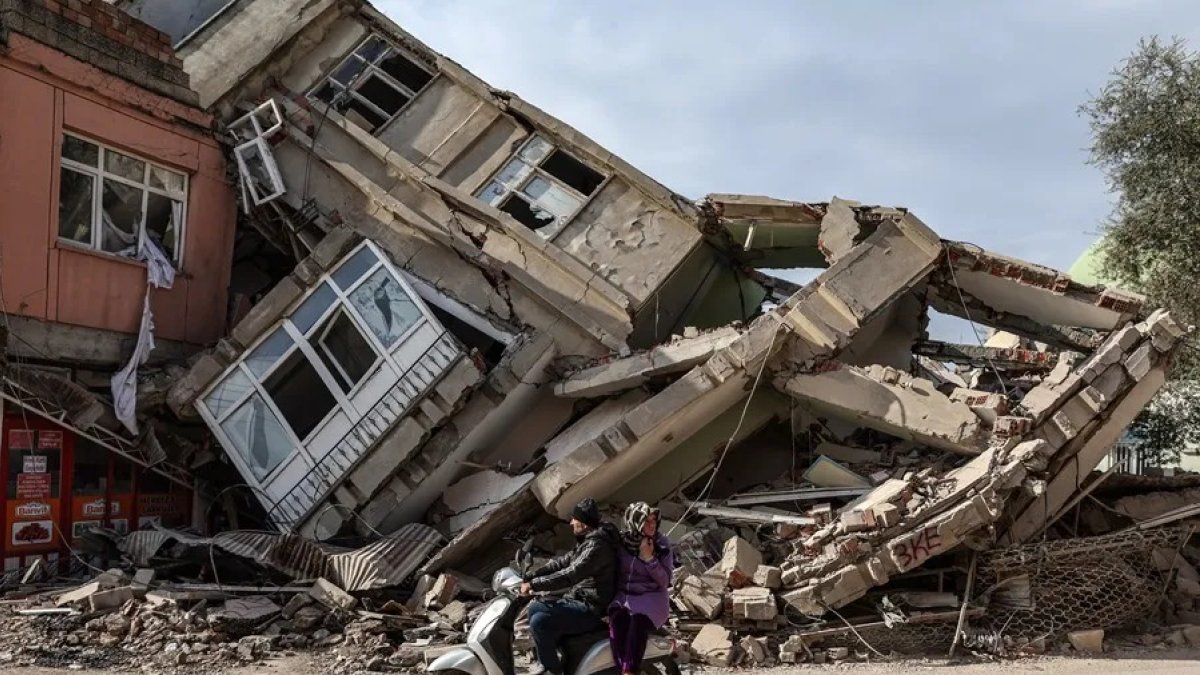 Varias personas pasan con una moto frente a un edificio destruido por los terremotos de Turquía.