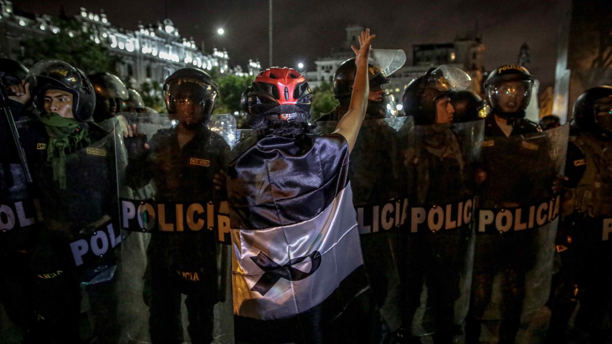 Un manifestante envuelto en una bandera peruana con color negro en lugar del rojo, se para frente a policías, en una fotografía de archivo.