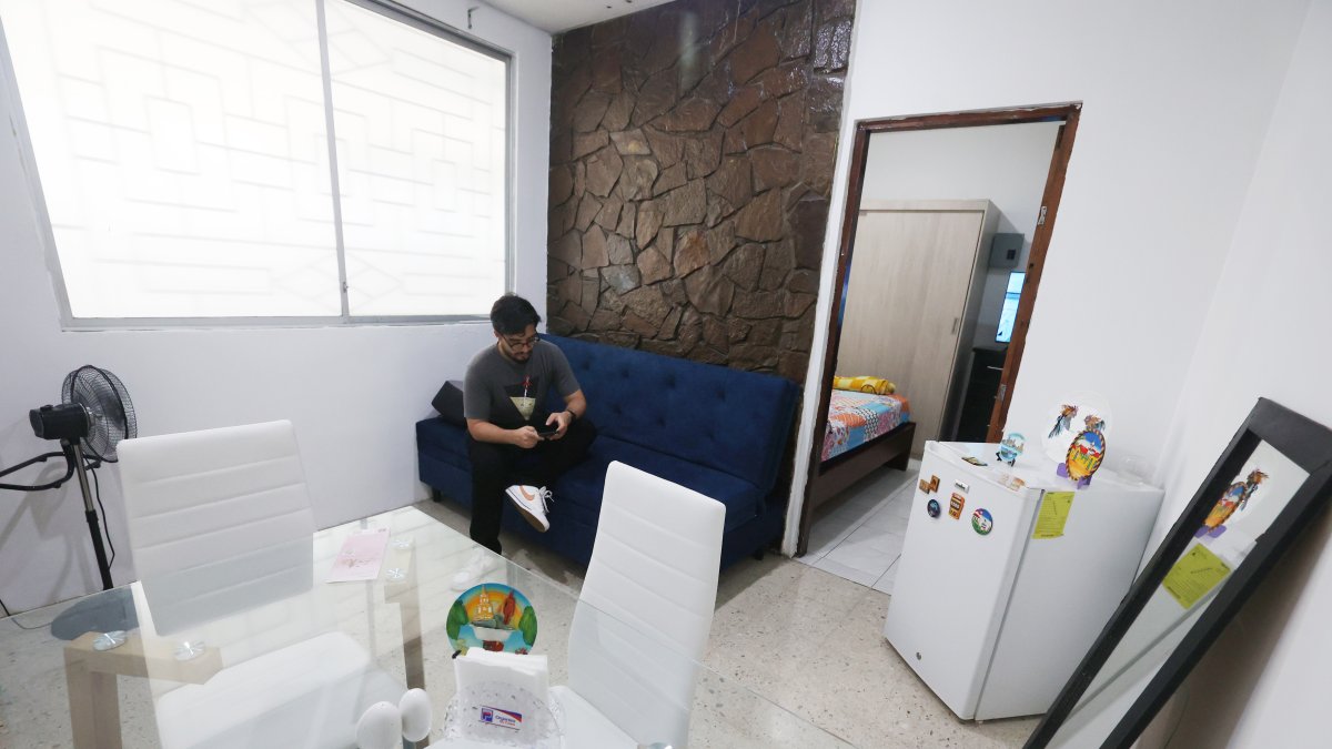 Departamento. Una persona está en su sala - comedor, que se ve pequeña, así como el dormitorio.
