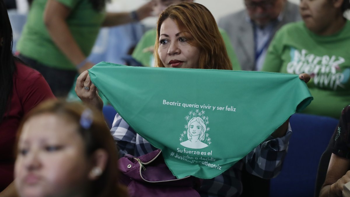 Una mujer muestra hoy una pañoleta verde con la imagen de Beatriz, mientras observa la transmisión en vivo de una audiencia de la CorteIDH, en San Salvador (El Salvador).