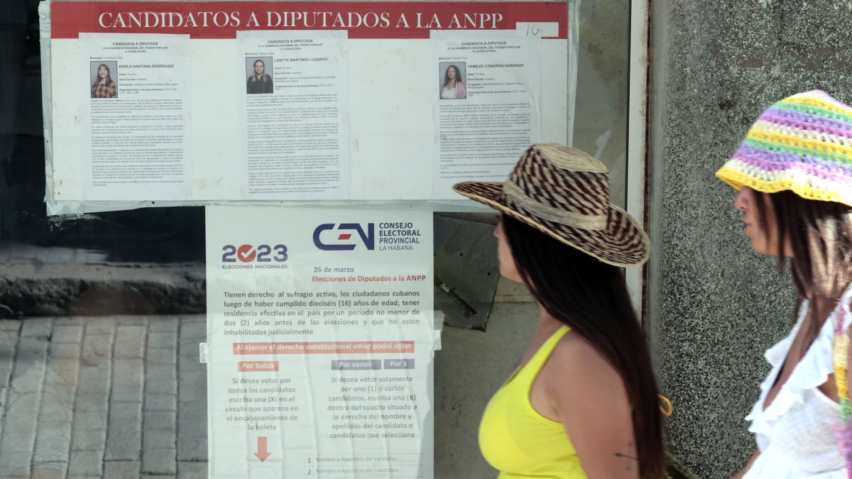 Dos mujeres pasan frente a unos carteles informativos sobre el proceso electoral del domingo.
