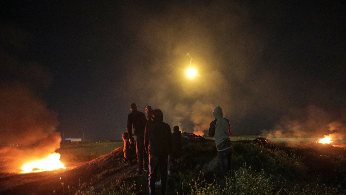 Los palestinos observan un cohete disparado hacia Israel mientras se reúnen entre neumáticos en llamas cerca de la frontera con Israel en Gaza.