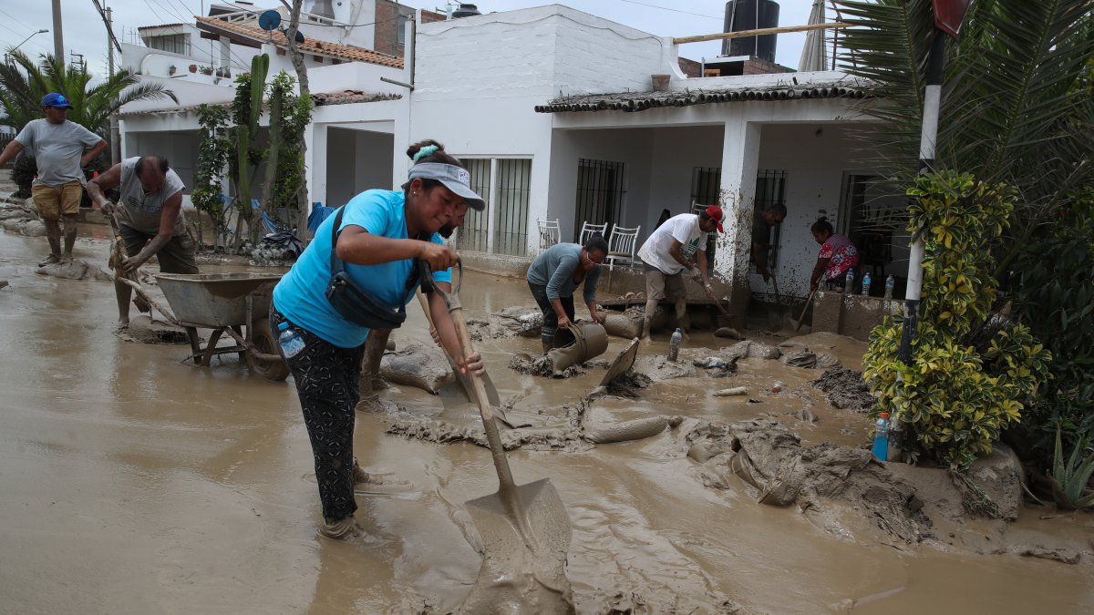 Personas ayudan a remover el lodo en una calle afectada por las lluvias, en el balneario de Punta Hermosa al sur de Lima (Perú), en una fotografía de archivo.