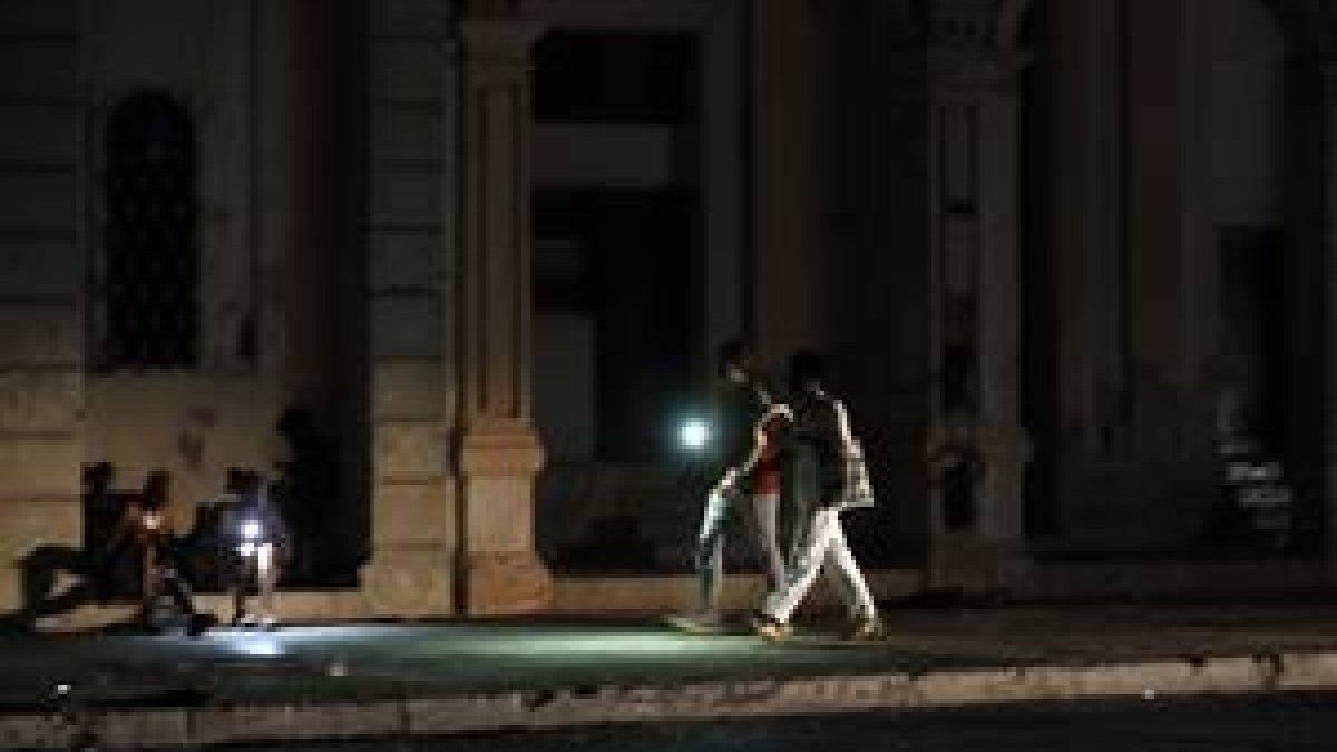 Personas caminan por una calle sin iluminación auxiliándose con la luz de su celular durante un apagón, en La Habana (Cuba).