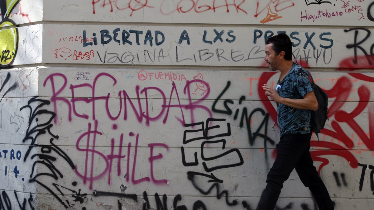 Un hombre camina frente a un mural pidiendo 