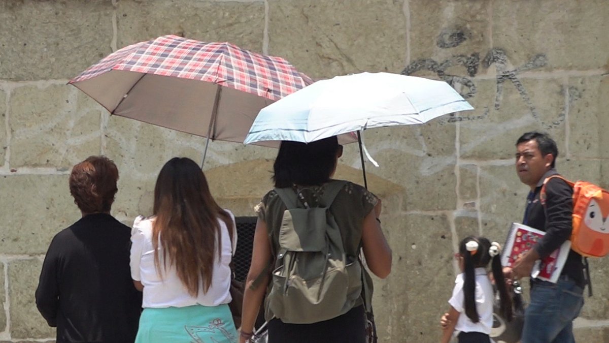 Unas mujeres se cubren con sombrillas del fuerte calor hoy 9 de mayo de 2023 en Oaxaca (México). 