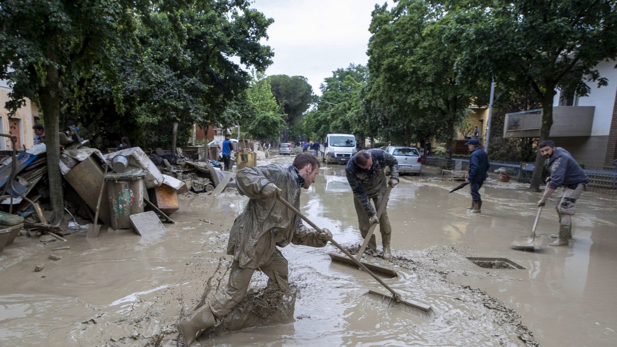 Personas trabajan para limpiar una calle anegada tras las inundaciones que están afectando a la región de Emilia-Romaña, en Faenza, Italia, el 19 de mayo de 2023.