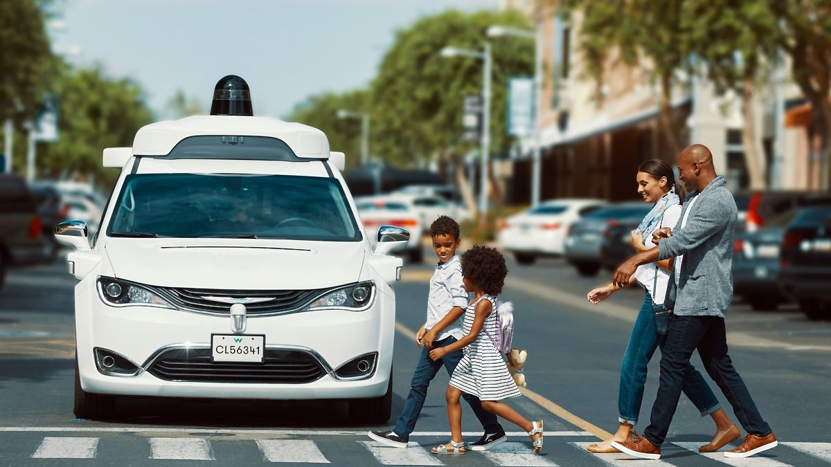 Algunas personas utilizan un paso cebra mientras una unidad sin conductor de Waymo, espera el cambio de luz.