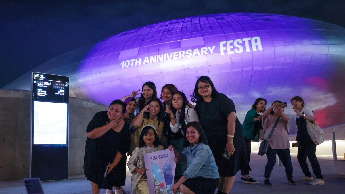 Turistas extranjeros se toman una foto frente a Dongdaemun Design Plaza en Seúl, Corea del Sur, iluminado de púrpura la noche del 12 de junio de 2023, como parte de un festival de dos semanas para celebrar el décimo aniversario de la sensación mundial del K-pop BTS debut, que cae el 13 de junio.