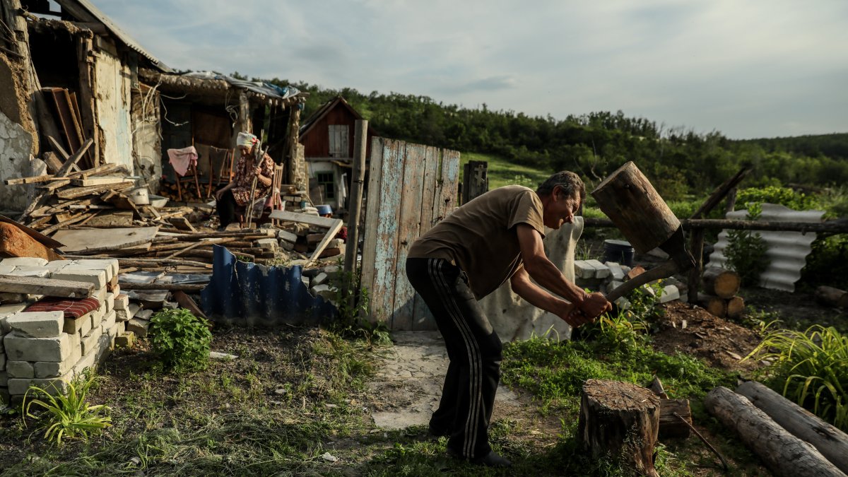 Mykola (R), de 58 años, corta leña mientras su madre Nina, de 92, se sienta en su patio entre los restos de su casa en el pueblo de Bohorodychne, región de Donetsk, Ucrania
