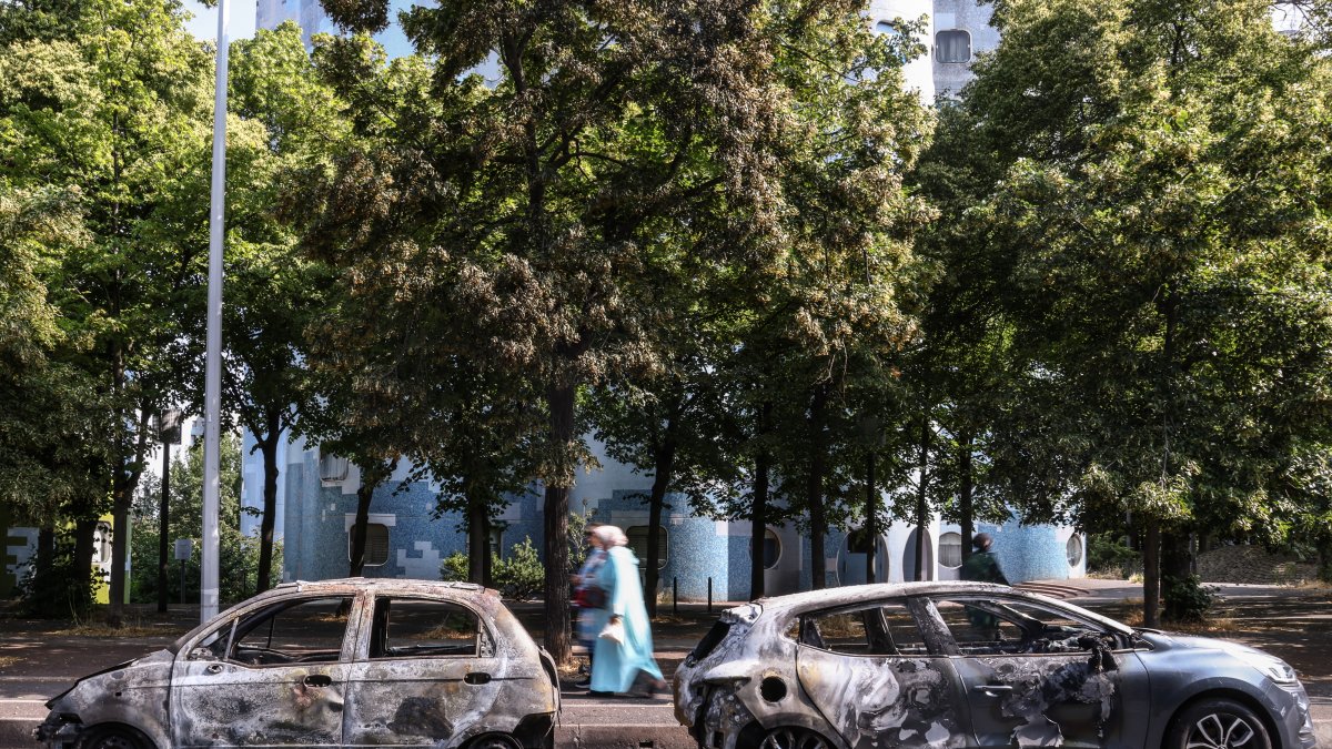 La gente pasa por delante de un coche incendiado en la avenida Pablo Picasso tras una noche de disturbios civiles, en Nanterre, cerca de París, Francia, el 28 de junio de 2023.