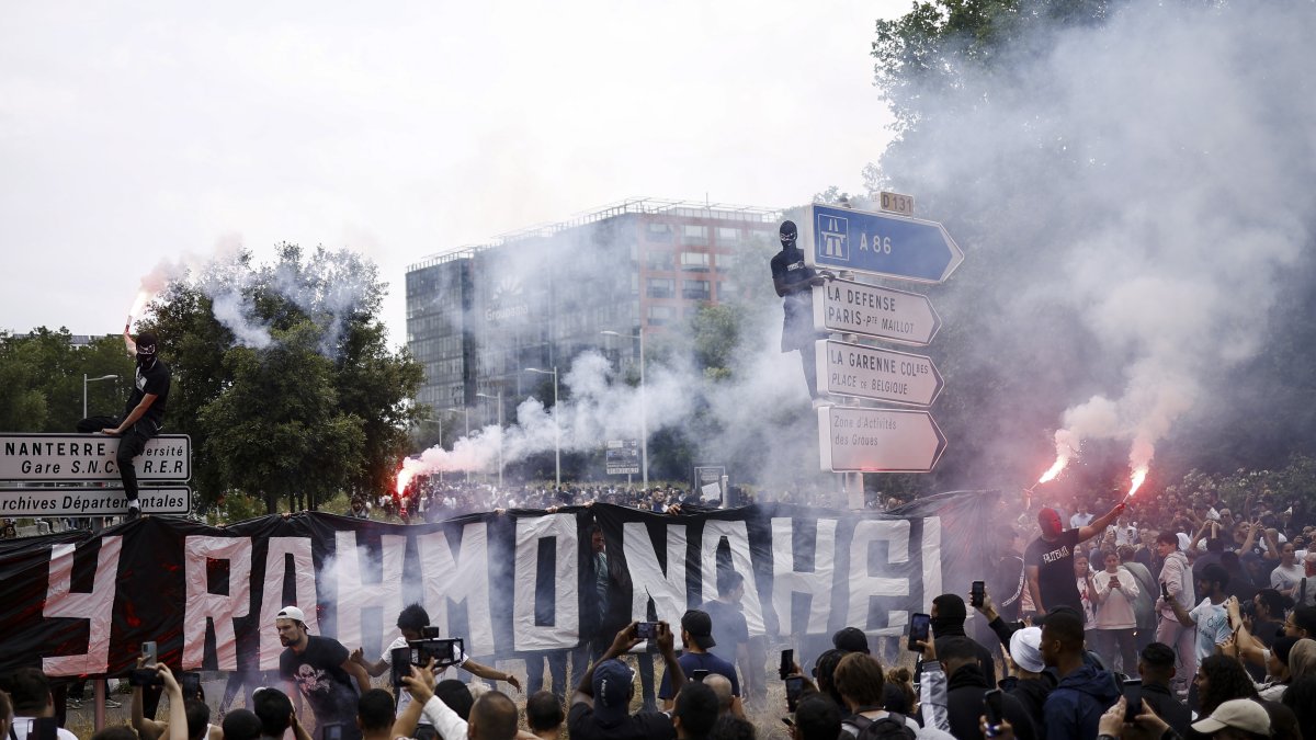 Un manifestante vestido de negro se ve en lo alto de una señal de tráfico, mientras la gente participa en una marcha en memoria de Nahel, de 17 años, asesinado por la policía francesa en Nanterre..