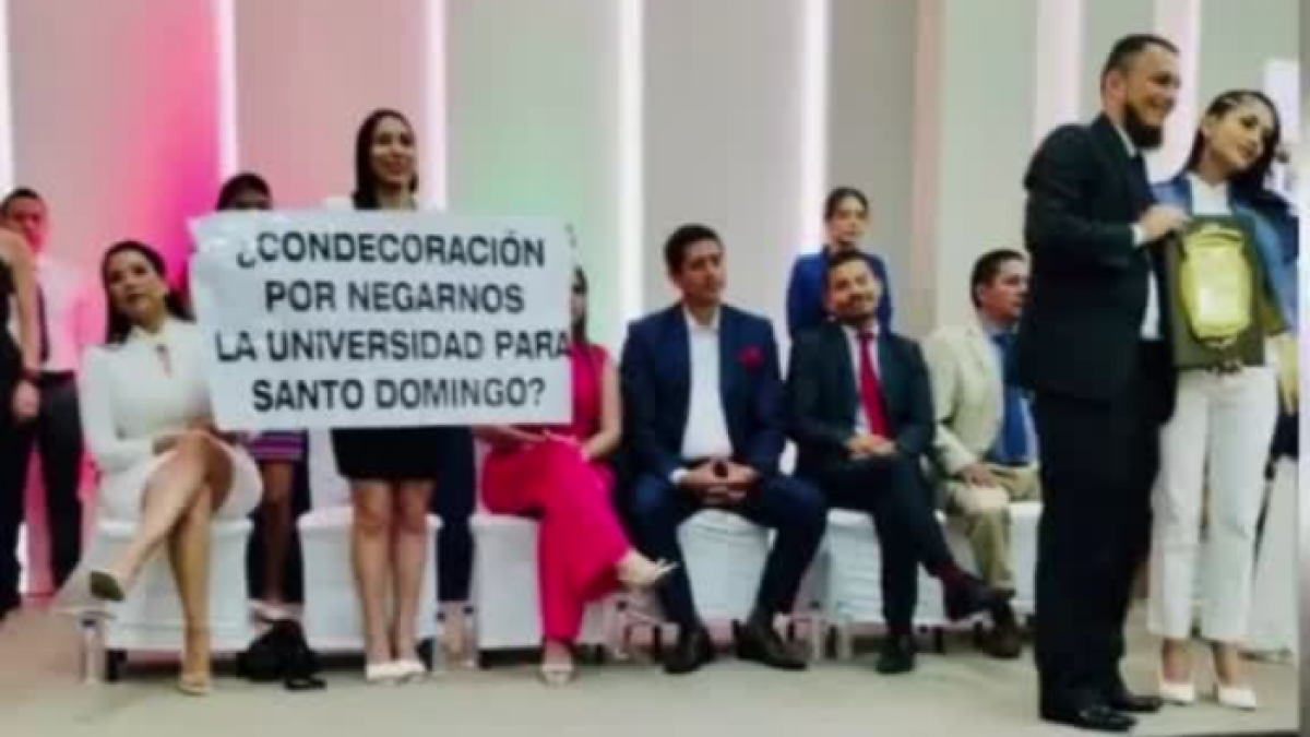 Liliana Silva sostiene un cartel de rechazo, mientras Viviana Veloz (der.) es reconocida en Santo Domingo